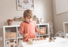 Wooden Educational Toys boy in orange crew neck t-shirt standing in front of white wooden table with cupcakes