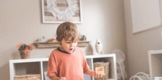 Wooden Educational Toys boy in orange crew neck t-shirt standing in front of white wooden table with cupcakes