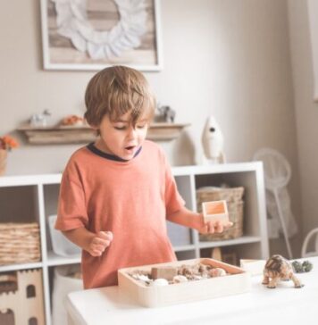 Wooden Educational Toys boy in orange crew neck t-shirt standing in front of white wooden table with cupcakes