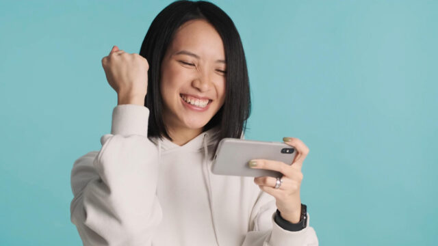 excited-asian-woman-emotionally-playing-mobile-phone-celebrating-win-online-game-isolated-blue-background