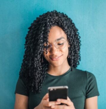 The Intrigues of Political Betting in the Modern Age Portrait Photo of Smiling Woman in Black T-shirt and Glasses Using Her Smartphone
