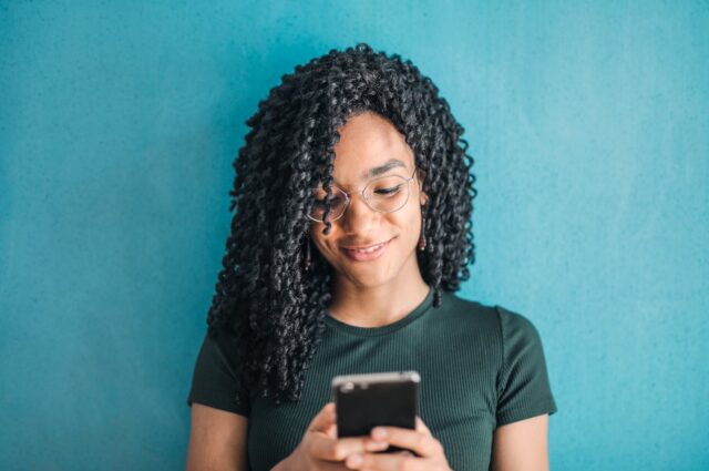 Photo by Andrea Piacquadio Portrait Photo of Smiling Woman in Black T-shirt and Glasses Using Her Smartphone