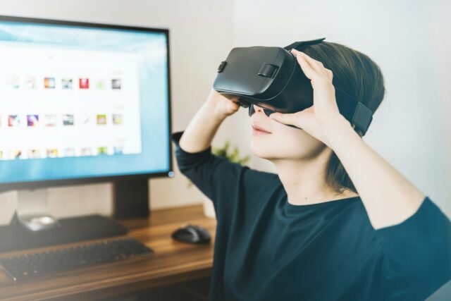 Photo by JESHOOTS.COM woman using black VR headset beside computer